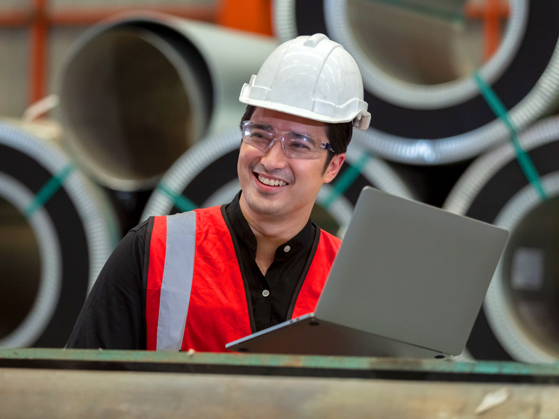 Factory worker smiling using laptop on the shop floor with maintained Infor applications