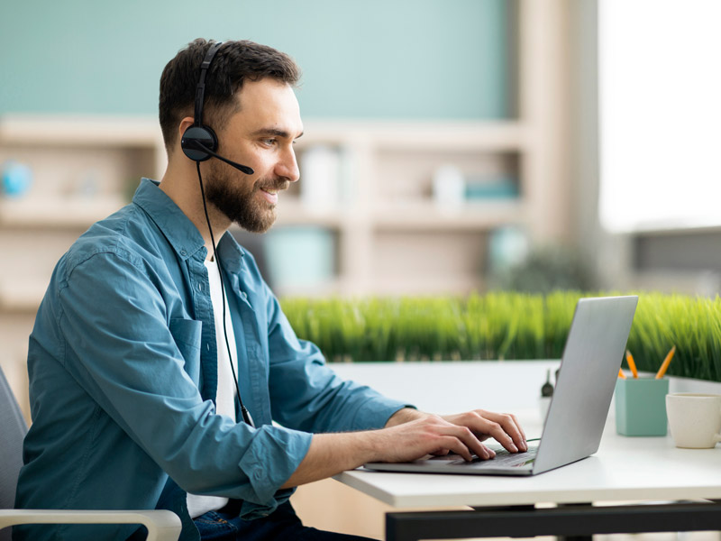 Flexible support worker answers customer call while working remotely on a laptop