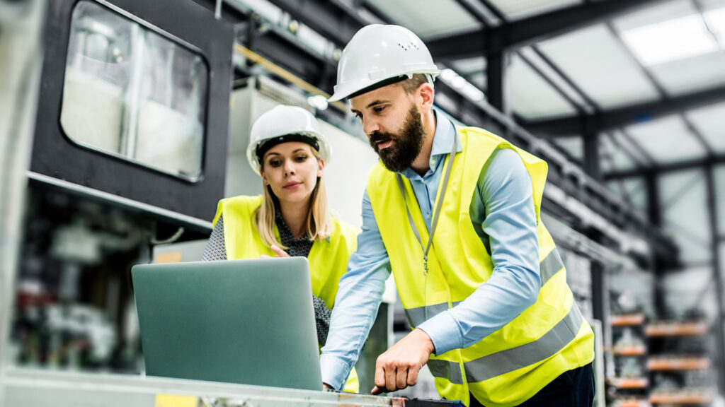 Two-Factory-Workers-Reviewing-Manufacturing-Data-on-Laptop