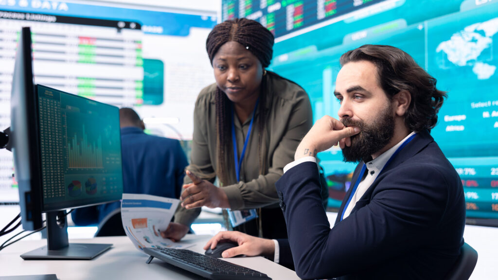 Two-Finance-Workers-Reviewing-Data-On-Desktop-Computer