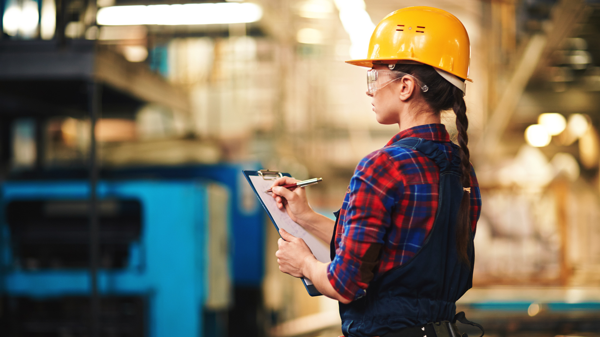 Female worker looks at manufacturing machinery and analysing rising costs